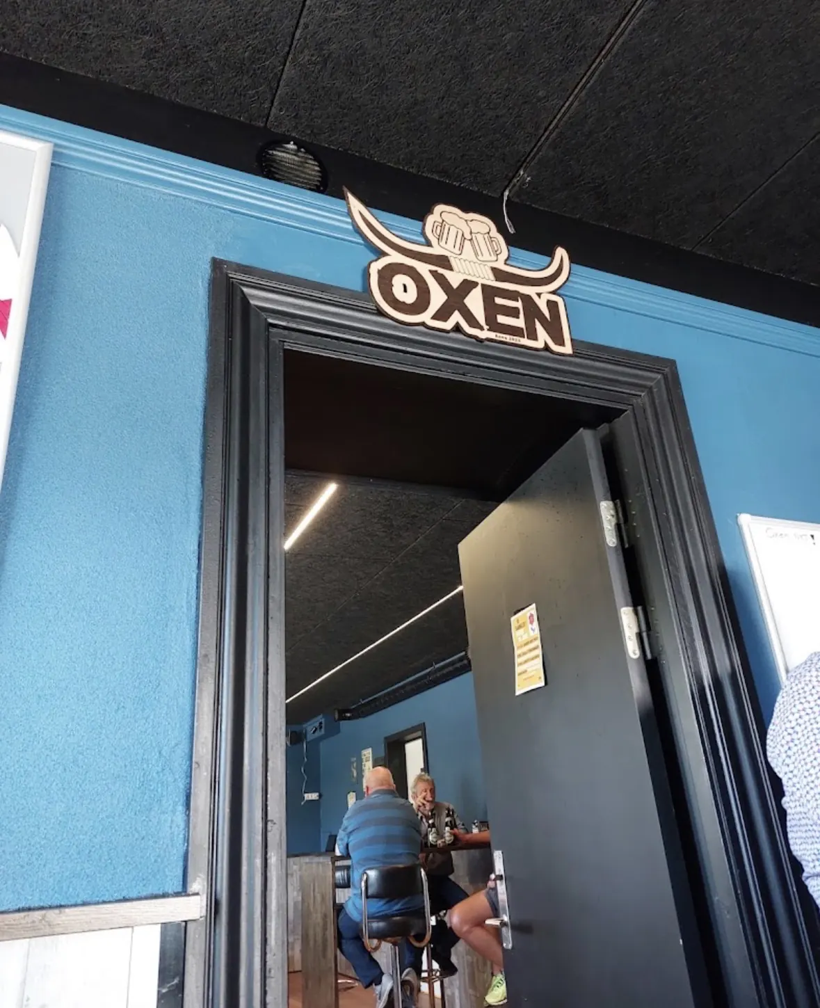 Indgangen til Oxen med det udskårne Oxen-skilt over døren og gæster ved baren